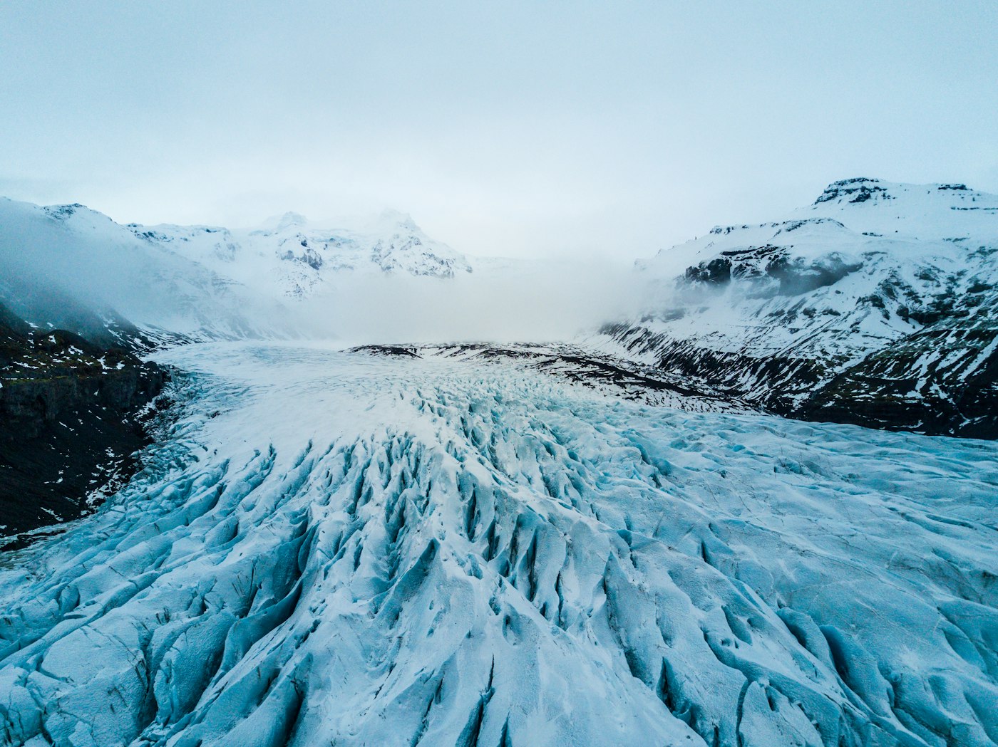 A glacier flowing between snow-covered mountains
